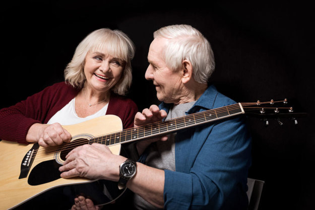 portrait of smiling senior couple holding guitar on black