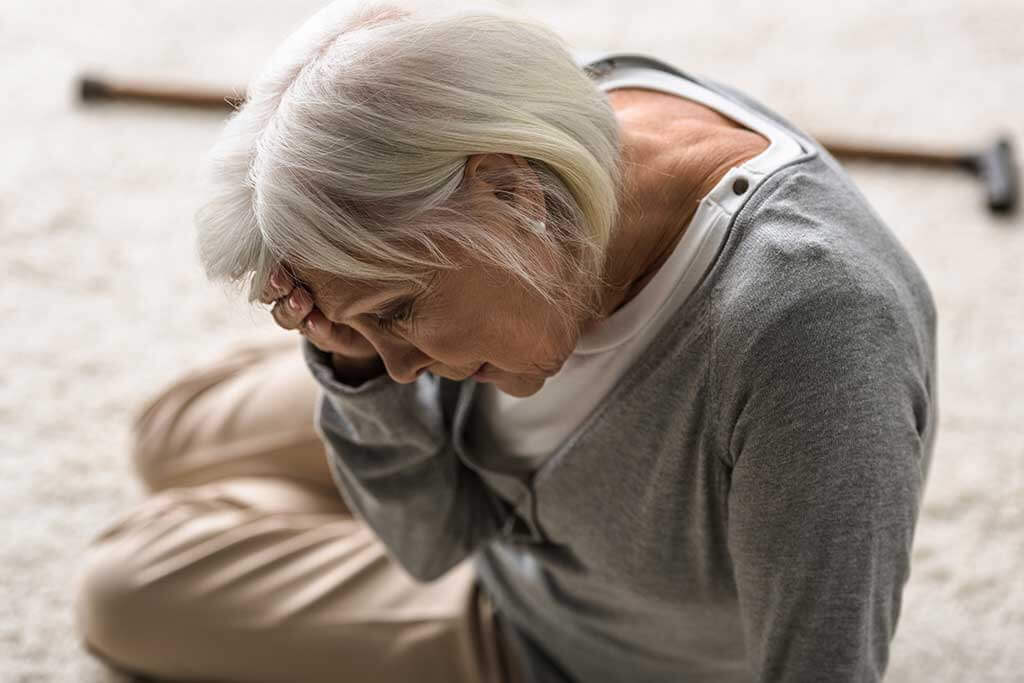 senior woman with migraine sitting on carpet and touching forehead with hand senior woman with migraine sitting on carpet and touching forehead with hand