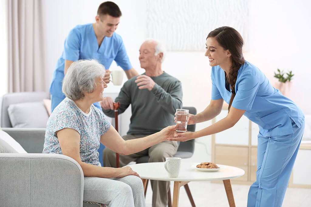 young caregiver giving glass of water to senior woman indoors