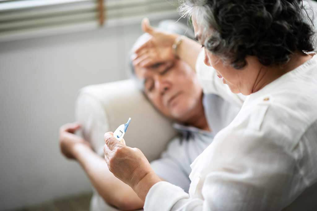 asian senior man lying on sofa while his wife holding and looking to thermometer asian senior man lying on sofa while his wife holding and looking to thermometer