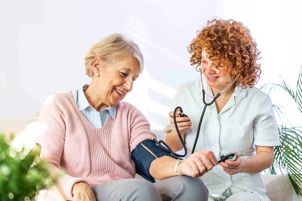 happy nurse measuring blood pressure of a senior woman