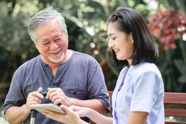 nurse with patient sitting on bench together looking at tablet