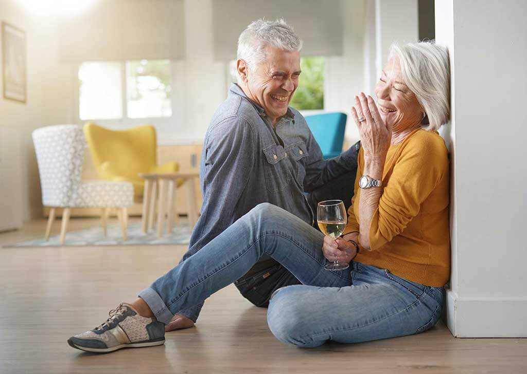 relaxed senior couple sitting on floor in modern home with glass of wine