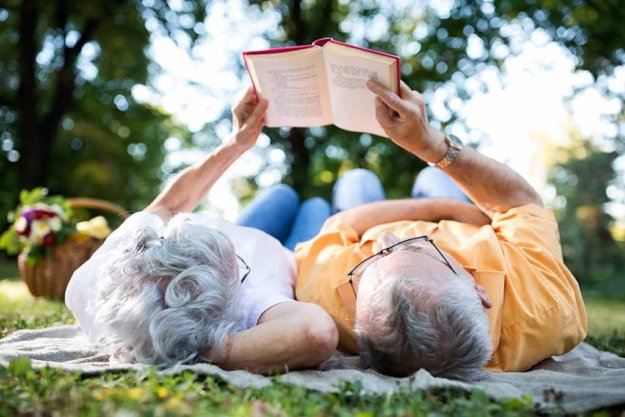 senior couple resting at park reading a book