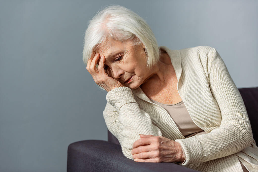 senior lonely woman holding hand on face while sitting on sofa senior lonely woman holding hand on face while sitting on sofa