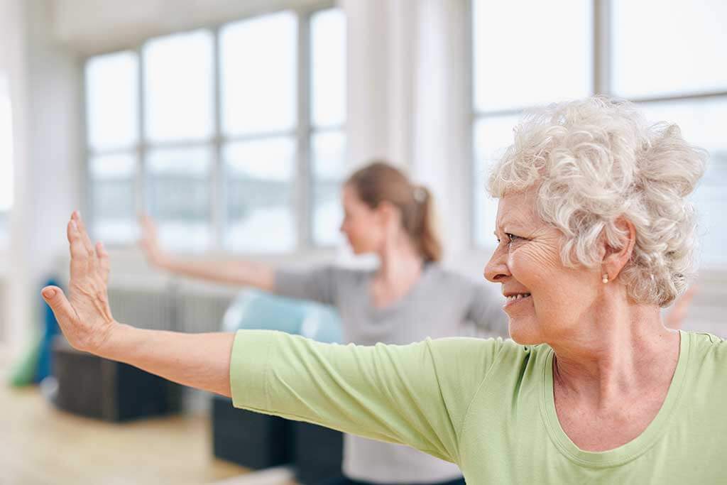 senior woman doing stretching exercise at yoga class