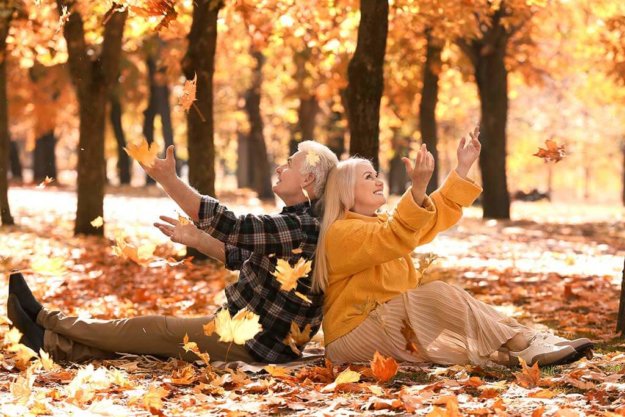 loving mature couple throwing leaves in autumn park