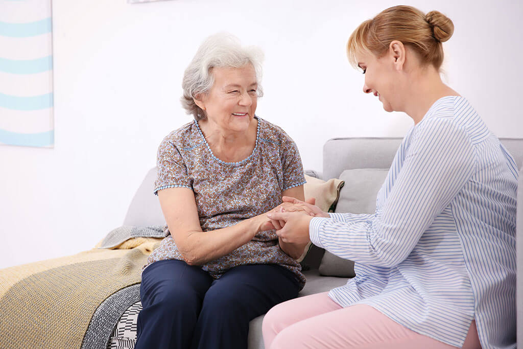 senior woman and caregiver sitting on sofa