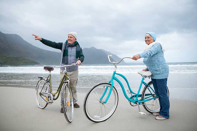 senior couple standing with bicycles on the beach senior couple standing with bicycles on the beach