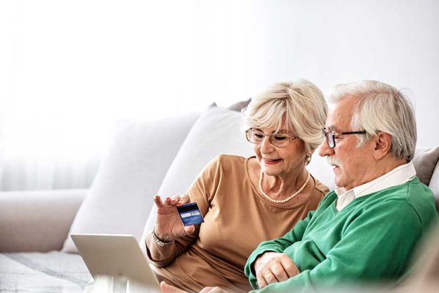 happy senior man buying stuff online with credit card next to wife in the living room happy senior man buying stuff online with credit card next to wife in the living room