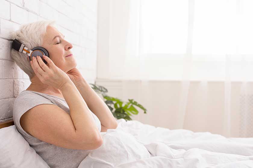 tranquil senior lady listening to audiobook in bed