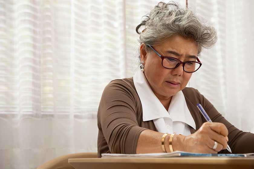 asian senior woman serious writing down letters on a piece of paper