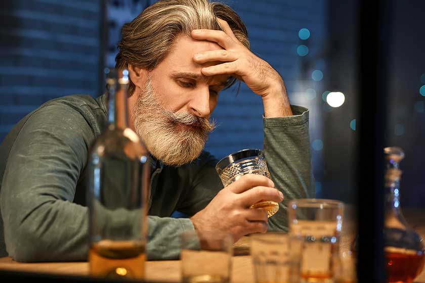 drunk senior man with glass of whiskey late in evening at home