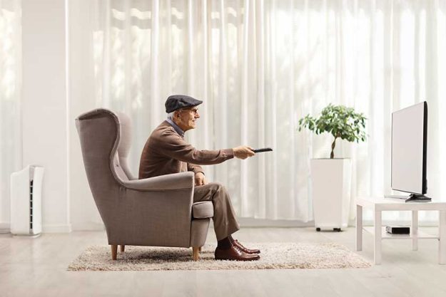 elderly man in an armchair changing channels on tv with remote control in a living room elderly man in an armchair changing channels on tv with remote control in a living room