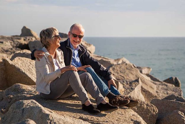 happy senior couple sitting on rocks by the sea