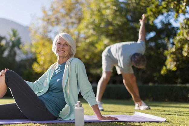 portrait happy senior woman on yoga mat in sunny park