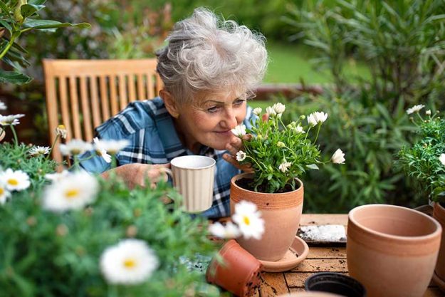 senior woman gardening on balcony in summer drinking coffee