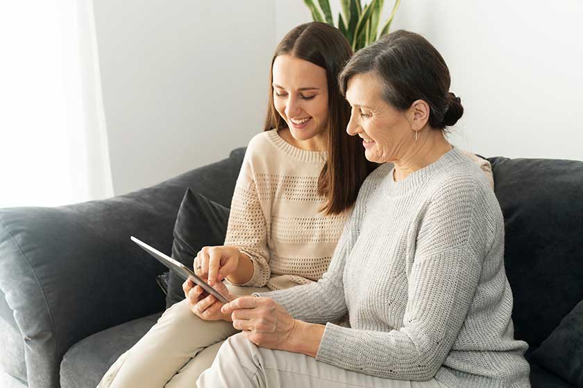 side view an adult daughter and a senior mother spend time with a tablet indoor