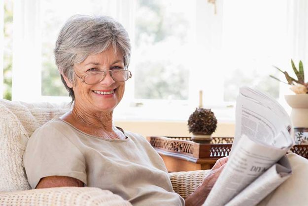 woman in living room reading newspaper smiling