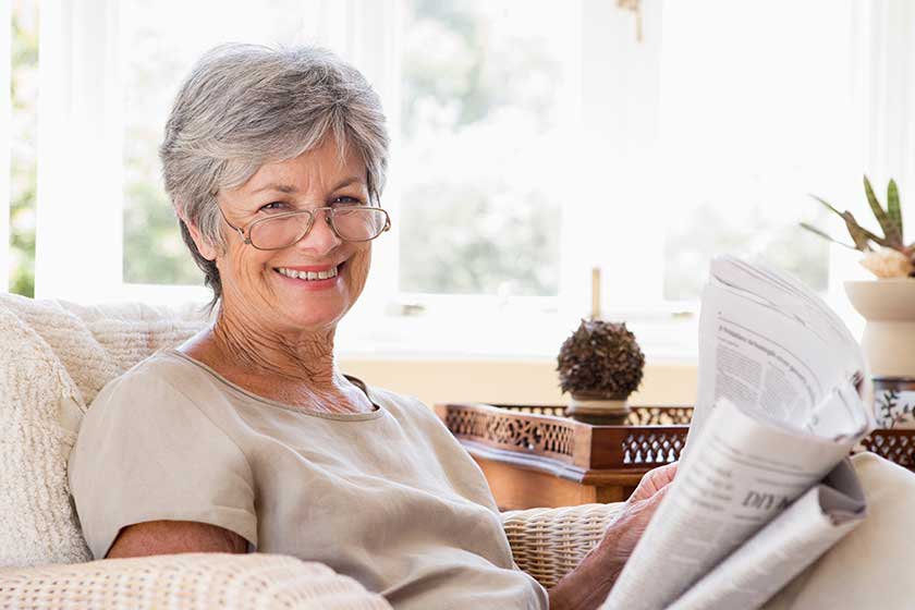 woman in living room reading newspaper smiling woman in living room reading newspaper smiling