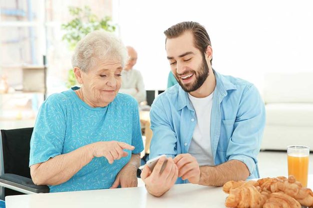 young caregiver teaching senior woman to handle with mobile phone at home young caregiver teaching senior woman to handle with mobile phone at home