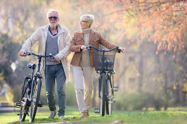 cheerful active senior couple with bicycles walking through park together