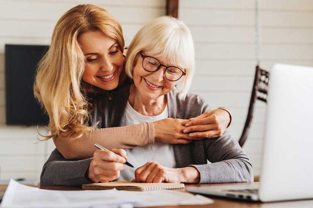 adult daughter helping senior woman complete form at home