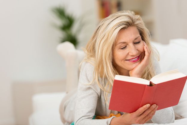 frau liegt auf dem sofa und liest ein buch
