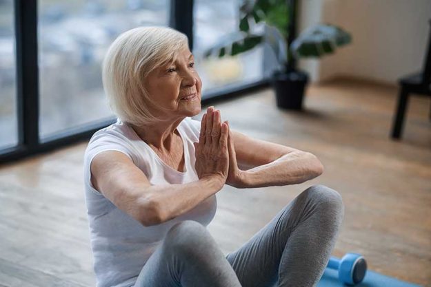 gray haired senior woman sitting on the floor and meditating