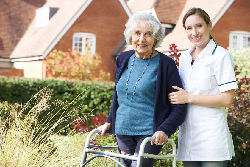 nurse helping senior woman use a walking frame