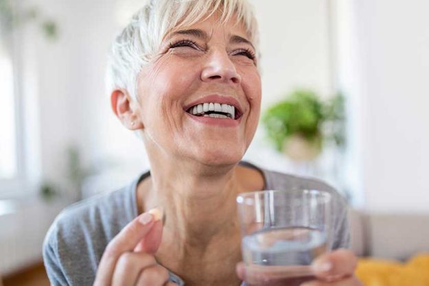 happy woman holds pill glass of water takes daily medicine