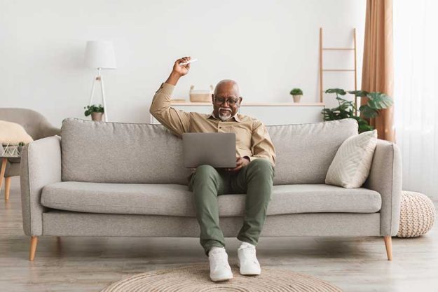 mature african man using laptop pointing remote controller up indoor