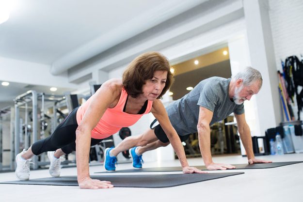 senior couple in gym working out doing push ups senior couple in gym working out doing push ups
