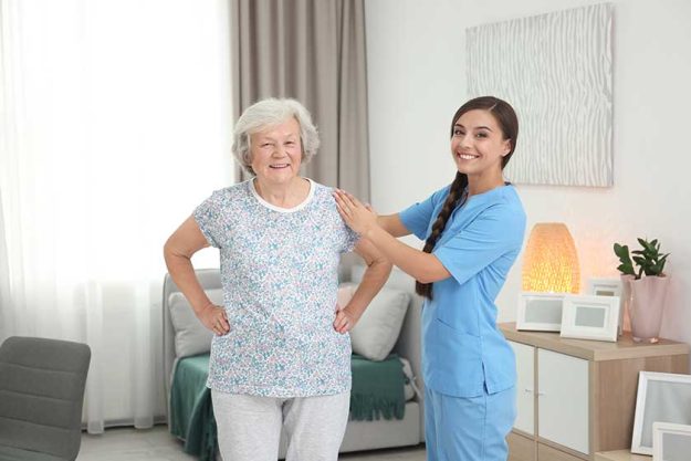 senior woman doing therapeutic gymnastics with assistance of young caregiver