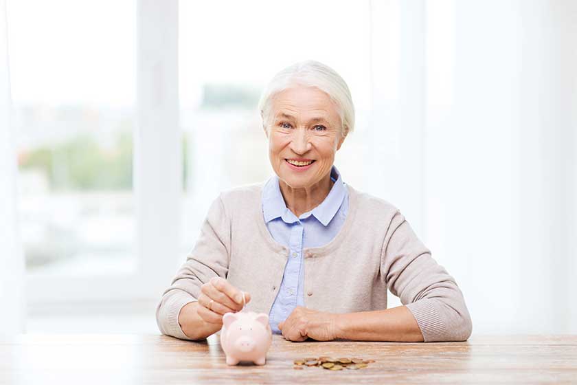 senior woman putting money to piggy bank at home