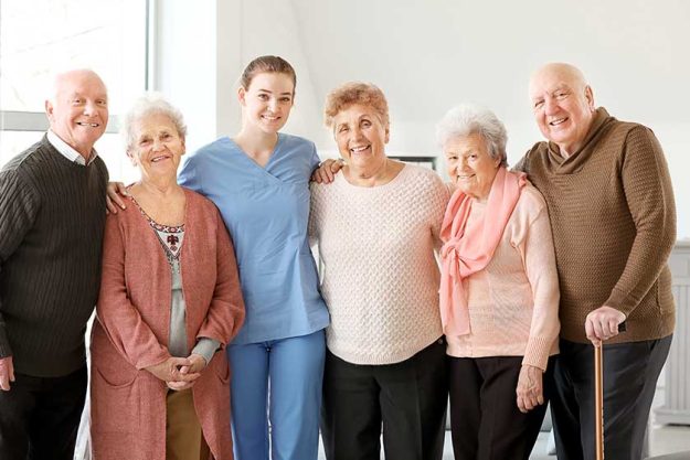 young caregiver with group of senior people in nursing home
