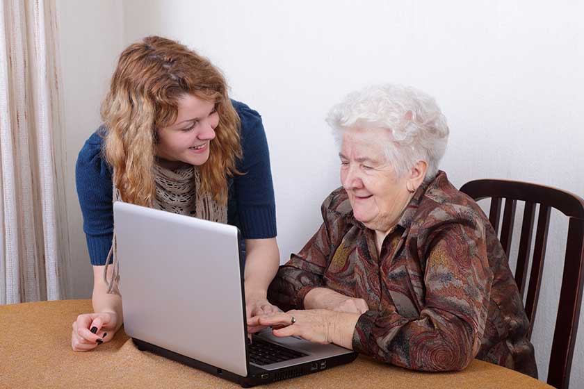 young girl teaching senior woman to work at computer