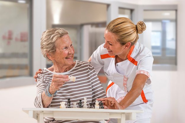 young homecarer playing chess with elderly woman