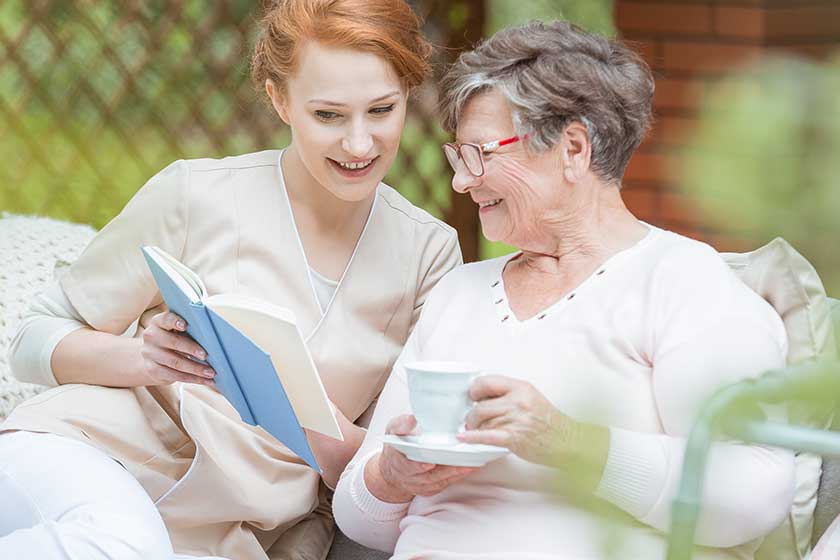 beautiful redhead nurse reads a book to elderly lady in the garden