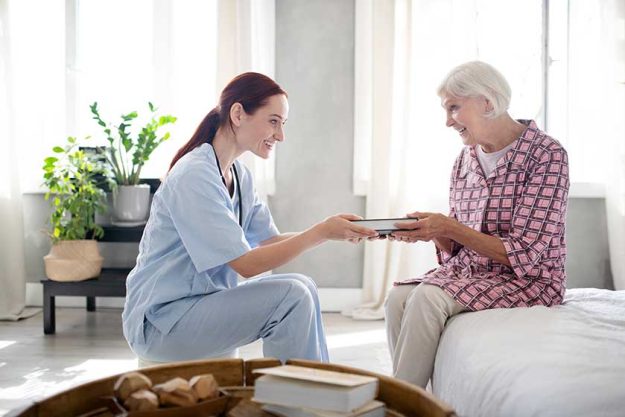 caring nurse smiling while giving book to aged woman