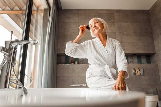 cheerful old lady looking out of the window and combing hair