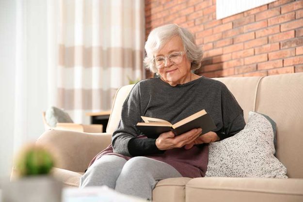 elderly woman reading book on sofa in living room