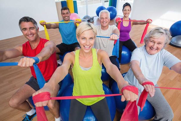 happy people exercising with resistance bands in gym