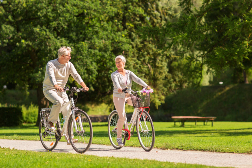 happy senior couple riding bicycles at summer park