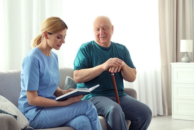 nurse reading book to elderly man indoors 1