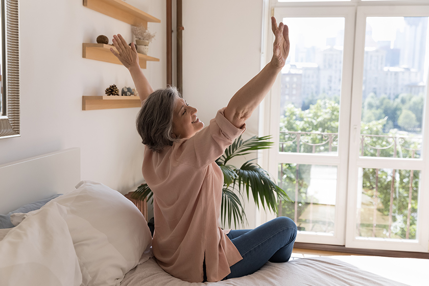 older woman sit on bed in modern light warm bedroom
