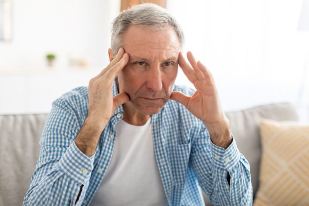 senior man sitting on sofa at home suffering from depression