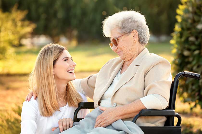 senior woman in wheelchair and nurse from care home outdoors