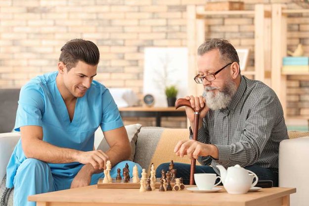 young caregiver and senior man playing chess at home