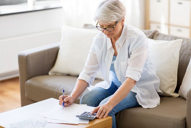 senior woman with papers or bills and calculator writing at home